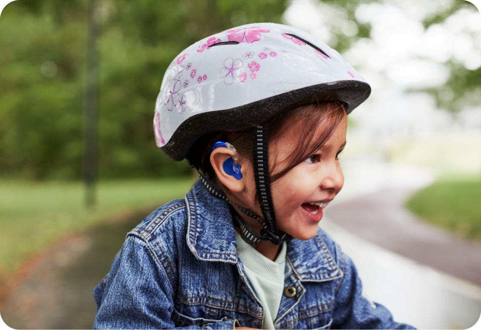 little girl with blue hearing aid and bike helmet boy cheering in a classroom full of kids
